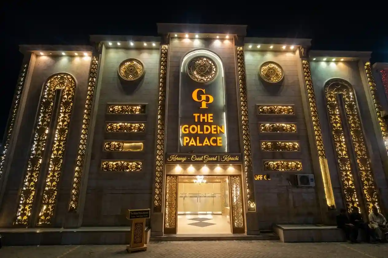 A wide, professional night photograph of the five-arch facade of The Golden Palace Banquet hall in Korangi, Coast Guard Karachi, featuring intricate gold jali screens, illuminated central signage with the 'GP' logo, and a bustling street scene